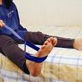 Body of a person sitting legs extended on a bed using a blue leg lifter