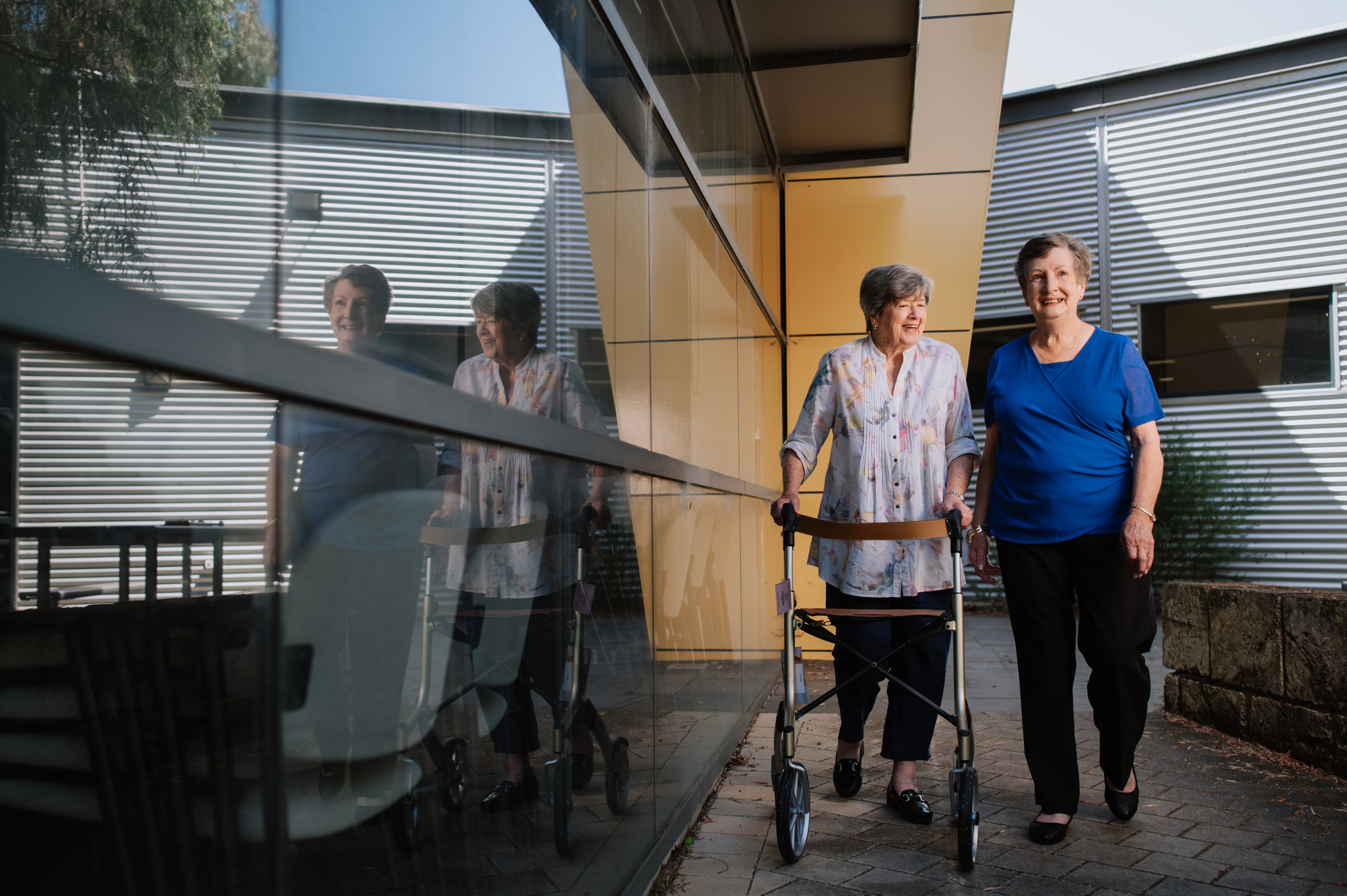 Two older females walking and chatting, one using a walker 