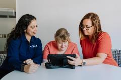 Female Indigo staff sitting with  two females using iPad in a room 