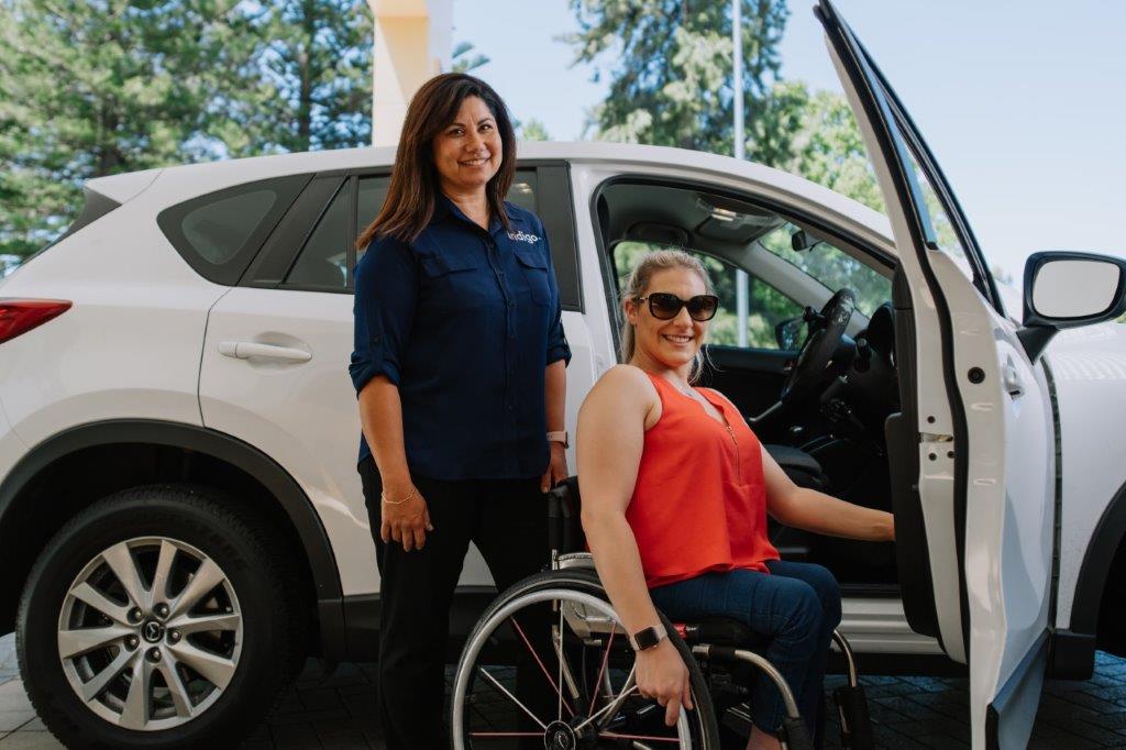 Female Indigo staff standing with female in wheelchair in front of white car
