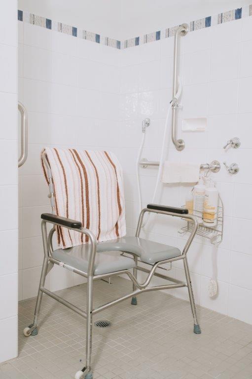 Shower chair with towel on back, adjustable shower head and wall handrails