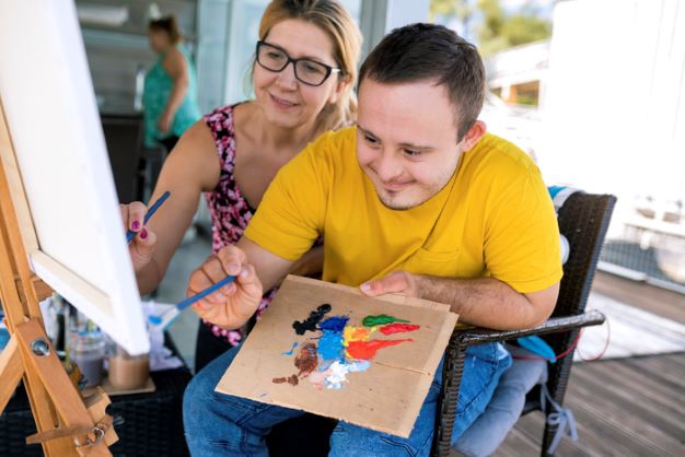 male with yellow shirt painting with support from older female