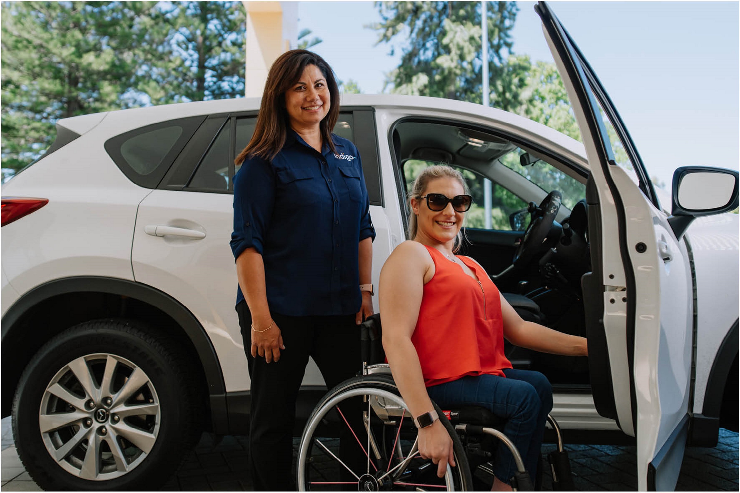 A female Indigo staff member is pictured in front of a car with an Indigo client who is using a wheelchair