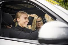Young female in car being shown how to driver by older female, both smiling