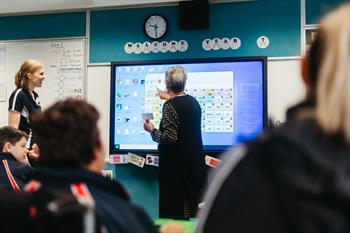 Classroom with focus on the teacher at the front using interactive whiteboard